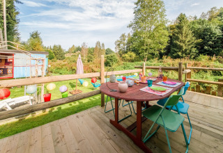 Wooden deck with colorful table setting overlooking nature at Les Roulottes de Vio mobile home in Belgium.
