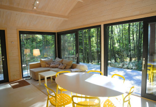 Moderne woonkamer in chalet ‘Droles d'écureuil’ in België met grote ramen en uitzicht op het bos.