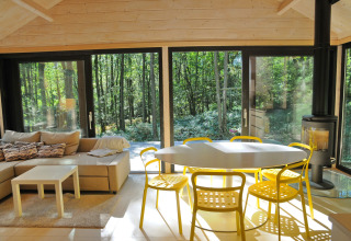 Lichte woonkamer in chalet 'Drôles d'écureuil' in België met gele stoelen en uitzicht op het bos.