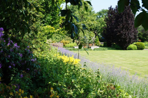 Jardin paysager avec pelouse bien taillée, fleurs colorées et arbres à un hébergement de glamping.