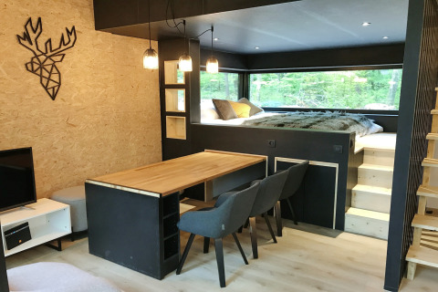 Modern lodge interior at Village de Vacances Oignies 5, Belgium, featuring dining area, bed and large window.