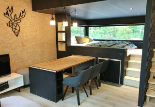 Modern lodge interior at Village de Vacances Oignies 5, Belgium, featuring dining area, bed and large window.
