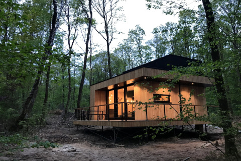 Modern wood lodge at dusk in the forest at Village de Vacances Oignies 5, Belgium, with warm interior lights.