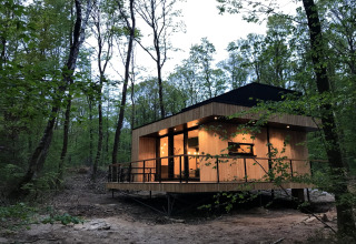 Modern wood lodge at dusk in the forest at Village de Vacances Oignies 5, Belgium, with warm interior lights.