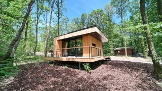 Modern houten vakantielodge op palen in een bosrijk gebied bij Village de Vacances Oignies 5 met blauwe hemel.