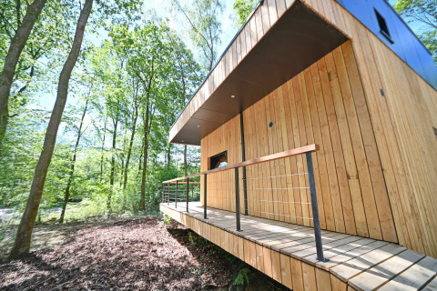 Modern wooden lodge with small terrace in the woods at Village de Vacances Oignies 5, Belgium, sunny day.
