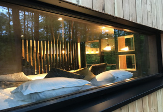 View through a window into the cozy interior of Village de Vacances Oignies 5 lodge, set in Belgian woods.