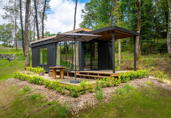 Moderne zwarte hut met ruim terras en parasol bij Hillview Resort Grandvoir 1, omringd door bos.