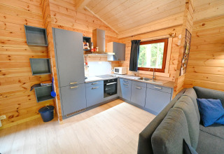 Cucina moderna in uno chalet di legno con armadi blu e divano al Village de Vacances Oignies 6, Belgio.