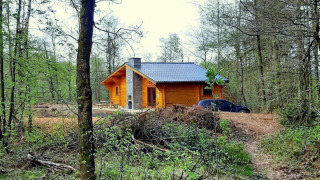 Chalet aus Holz im Village de Vacances Oignies 6, umgeben vom Wald, mit einem schwarzen Auto davor.