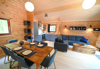 Interno chalet in legno con tavolo da pranzo, cucina e soggiorno al Village de Vacances Oignies 6, Belgio.