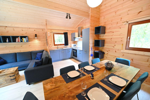 Accogliente soggiorno e cucina in chalet di legno presso Village de Vacances Oignies 6, Belgio, apparecchiato per sei.
