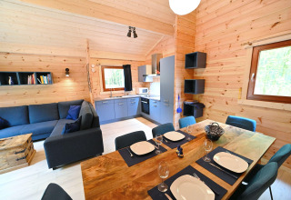 Accogliente soggiorno e cucina in chalet di legno presso Village de Vacances Oignies 6, Belgio, apparecchiato per sei.