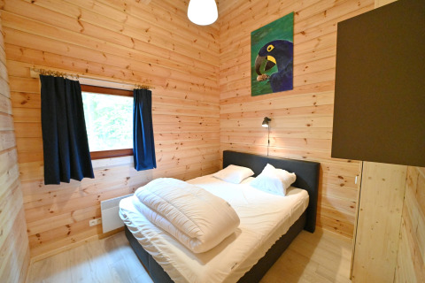 Camera da letto con pareti in legno, letto matrimoniale, finestra con tende scure e quadro di pappagallo.