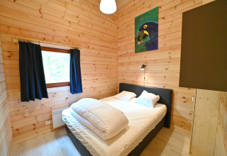 Camera da letto con pareti in legno, letto matrimoniale, finestra con tende scure e quadro di pappagallo.