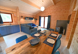 Interno di chalet al Village de Vacances Oignies 6 in Belgio con pareti in legno, divano, tavolo e stufa.