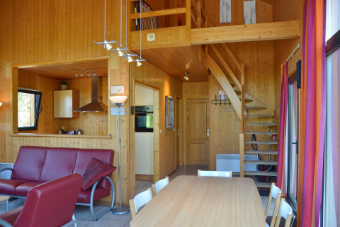 Indretning af en hyggelig, moderne hytte med træinteriør, køkken, spisebord, sofa og trappe til hems.