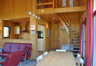 Indretning af en hyggelig, moderne hytte med træinteriør, køkken, spisebord, sofa og trappe til hems.