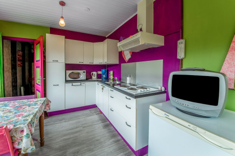 Colorful kitchen in a yurt with white cabinets, appliances, and retro TV at La Pause Insolite in Belgium.