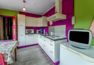 Colorful kitchen in a yurt with white cabinets, appliances, and retro TV at La Pause Insolite in Belgium.