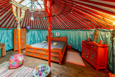 Interior of a colorful yurt named La Pause Insolite in Belgium, featuring ornate traditional decor and beds.