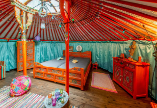 Interior of a colorful yurt named La Pause Insolite in Belgium, featuring ornate traditional decor and beds.