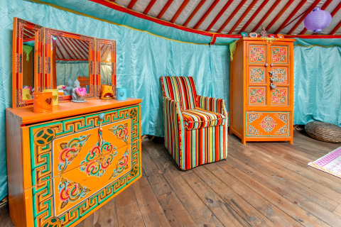 Colorful interior of a traditional yurt in Belgium, featuring ornate painted orange furniture and stripes.