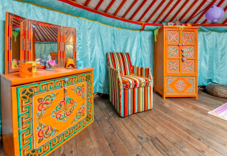Colorful interior of a traditional yurt in Belgium, featuring ornate painted orange furniture and stripes.