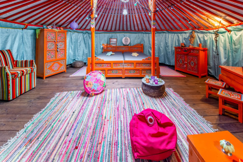 Colorful yurt interior with Mongolian decor, cozy furnishings and bed at La Pause Insolite in Belgium.