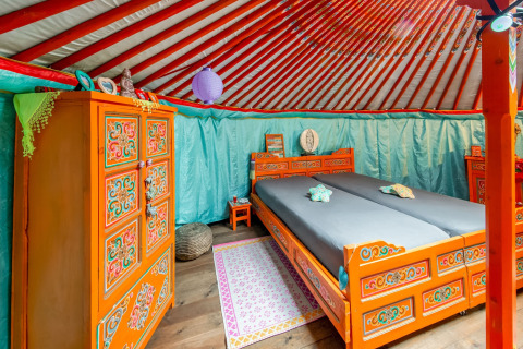 Interior of a colorful, ornately furnished yurt at La Pause Insolite in Belgium with decorated beds.