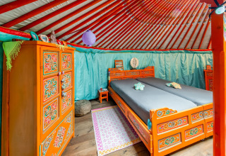 Interior of a colorful, ornately furnished yurt at La Pause Insolite in Belgium with decorated beds.