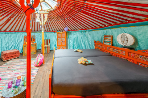 Colorful interior of a traditional yurt with double bed, furniture, and decor at La Pause Insolite, Belgium.