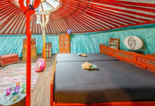 Colorful interior of a traditional yurt with double bed, furniture, and decor at La Pause Insolite, Belgium.