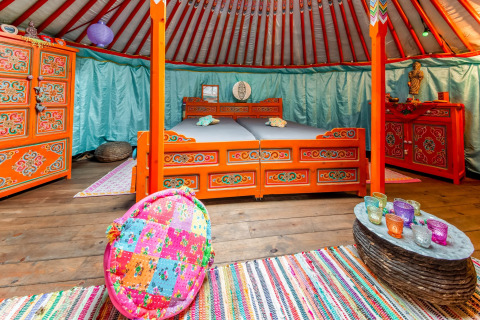 Colorful Mongolian yurt interior with traditional furniture and vibrant textiles at La Pause Insolite, Belgium.