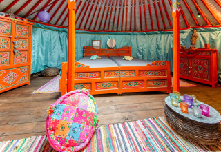 Colorful Mongolian yurt interior with traditional furniture and vibrant textiles at La Pause Insolite, Belgium.