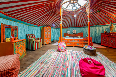 Colorful interior of a traditional yurt with vibrant furniture and rug in La Pause Insolite, Belgium.