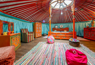 Colorful interior of a traditional yurt with vibrant furniture and rug in La Pause Insolite, Belgium.