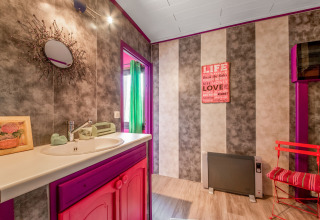 Colorful yurt bathroom in Belgium with pink and purple decor, mirror, striped walls, and quote art.