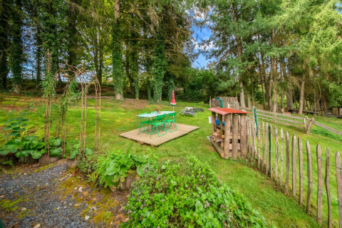 Garden area at La Pause Insolite yurt in Belgium with green chairs, a wooden deck, and tall trees.
