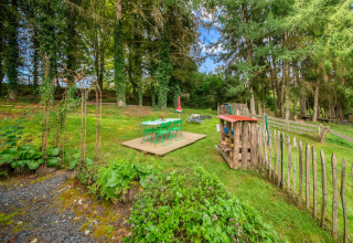 Garden area at La Pause Insolite yurt in Belgium with green chairs, a wooden deck, and tall trees.