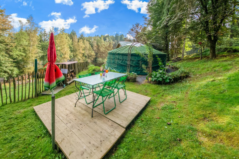 Outdoor dining area with green chairs by a yurt, surrounded by nature at La Pause Insolite in Belgium.