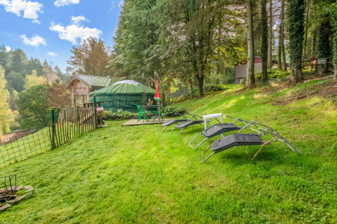 Yurt at La Pause Insolite in Belgium with loungers on a grassy lawn, surrounded by woods and trees.