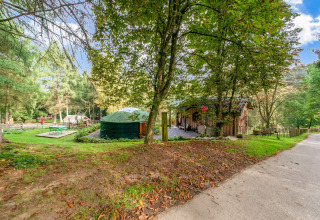 Photo of the yurt 'La Pause Insolite' in Belgium, set among trees, grassy lawn, and outdoor seating areas.