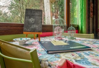 Cozy table setup inside yurt La Pause Insolite in Belgium, with birdcages, menu, and welcome board.