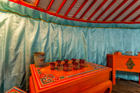 Interior of a traditional yurt at «La Pause Insolite» in Belgium, featuring ornately painted furniture.