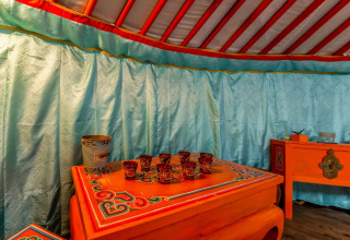 Interior of a traditional yurt at «La Pause Insolite» in Belgium, featuring ornately painted furniture.