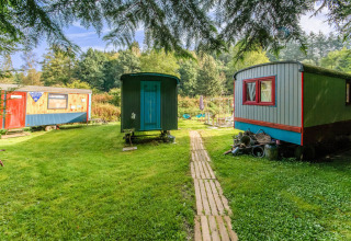 Colorful mobile homes set on a grassy lawn surrounded by trees at Les Roulottes de Vio in Belgium.