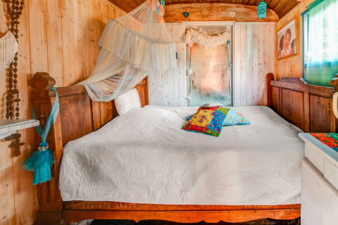 Cozy bedroom inside a mobile home at Les Roulottes de Vio, Belgium, with wood paneling and colorful pillows.
