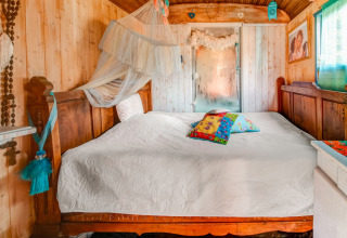 Cozy bedroom inside a mobile home at Les Roulottes de Vio, Belgium, with wood paneling and colorful pillows.
