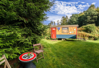 A cozy mobile home at Les Roulottes de Vio in Belgium, with outdoor seating and lush green surroundings.
